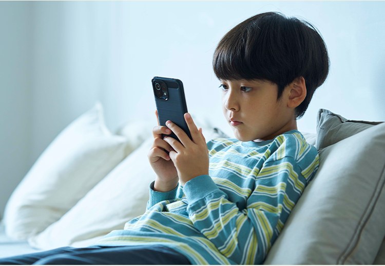 ソファでスマートフォンを見る子ども